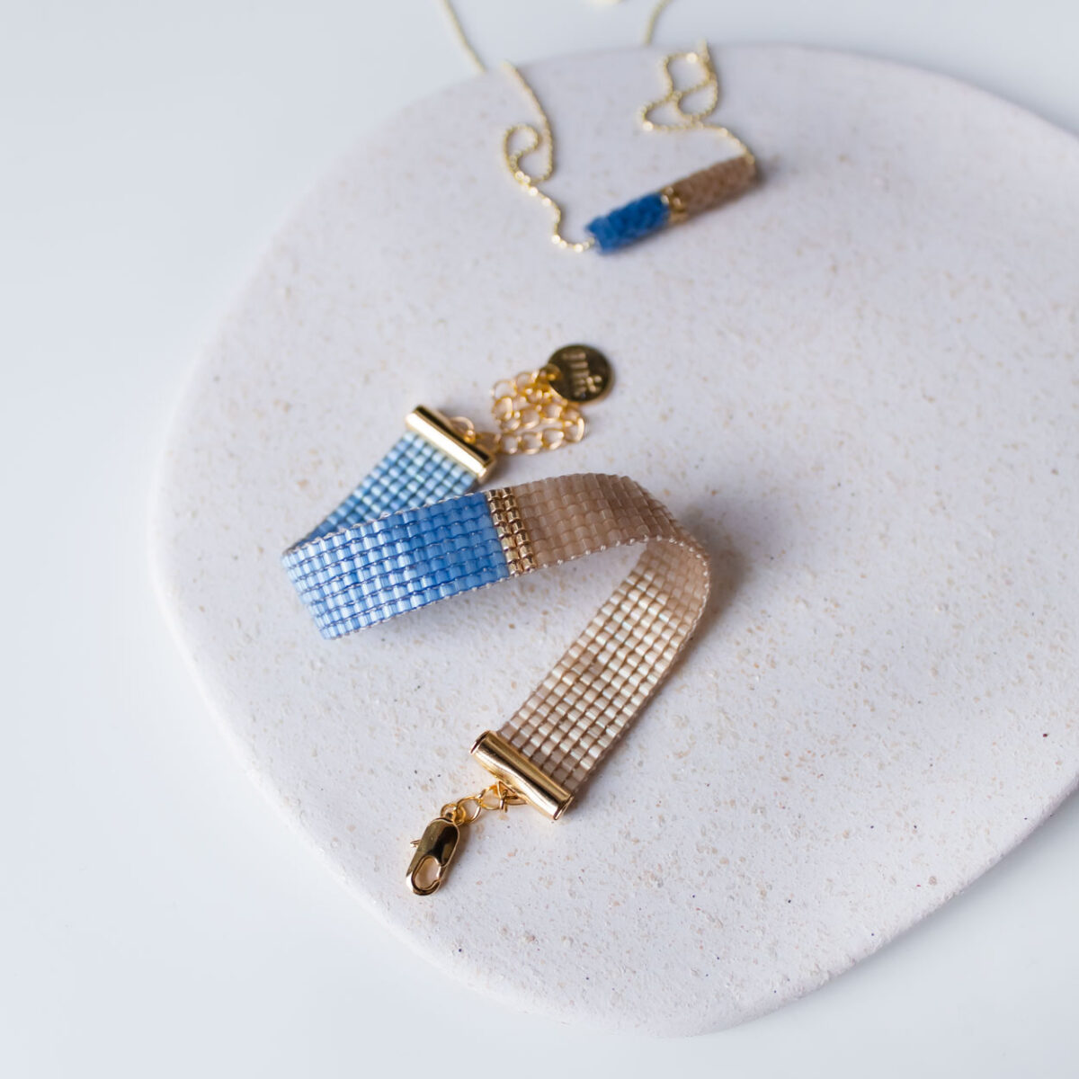 Elegant blue-beige bracelet and necklace displayed on a white ceramic plate.