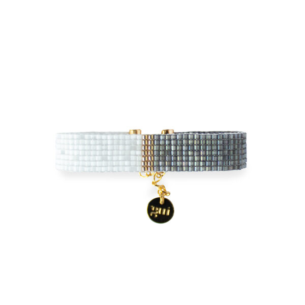 Elegant white and black beaded bracelet with a gold charm on a white background.