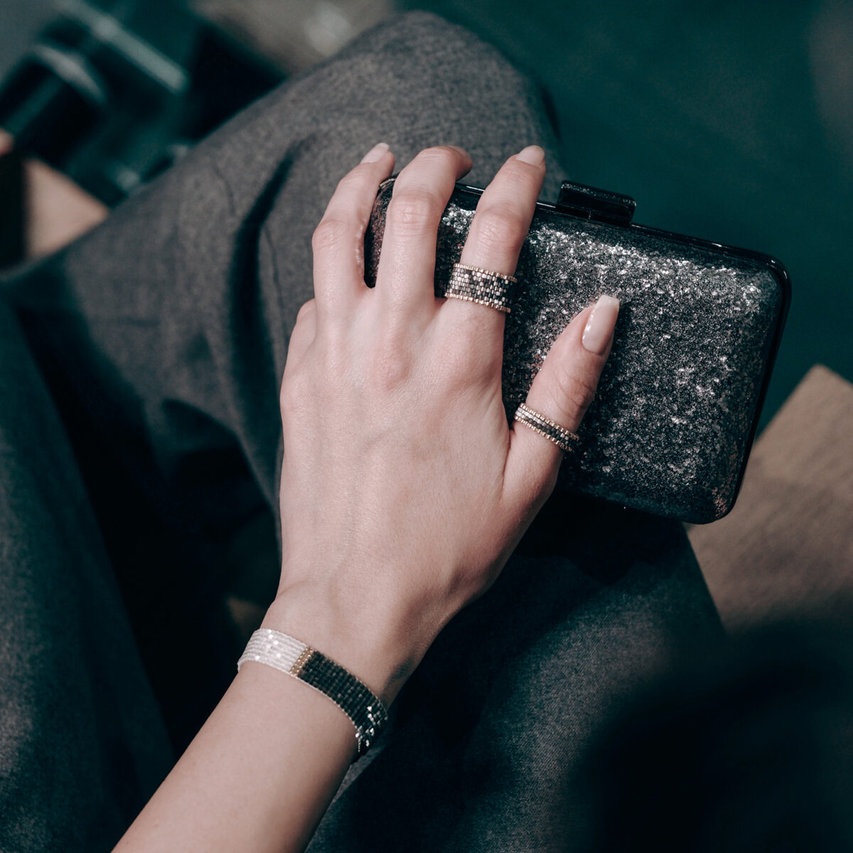 Close-up of a woman's hand with stylish glittery jewelry holding a black clutch purse.