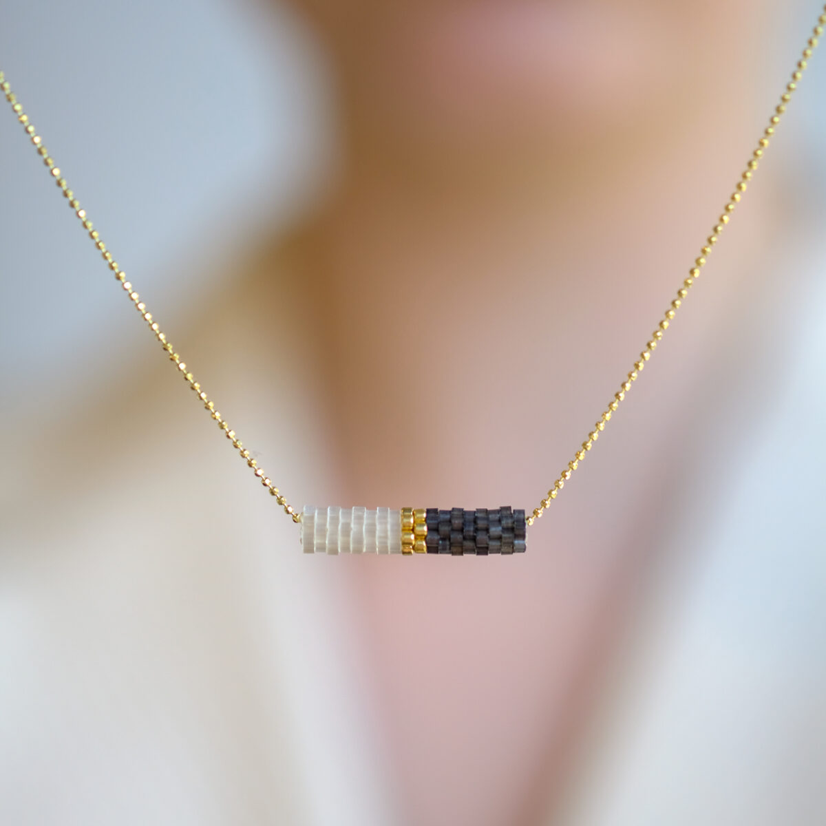 Elegant gold necklace with a bar of white, gold and black beads displayed on a blurred background.