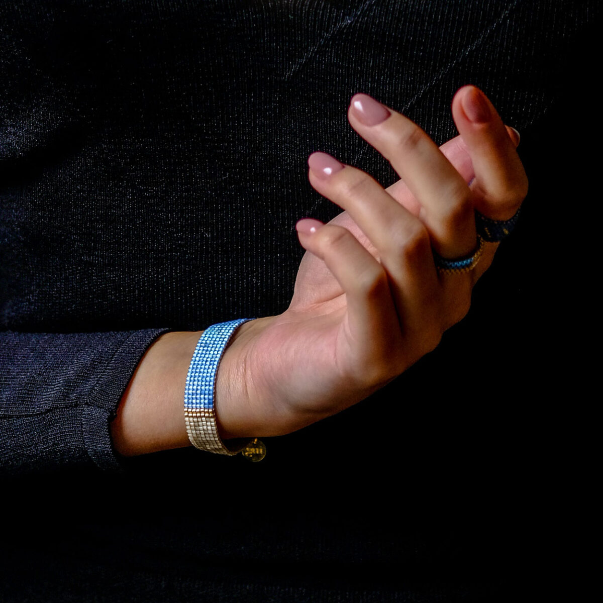 Close-up of a woman's hand and blue beaded bracelets against a black textured background.