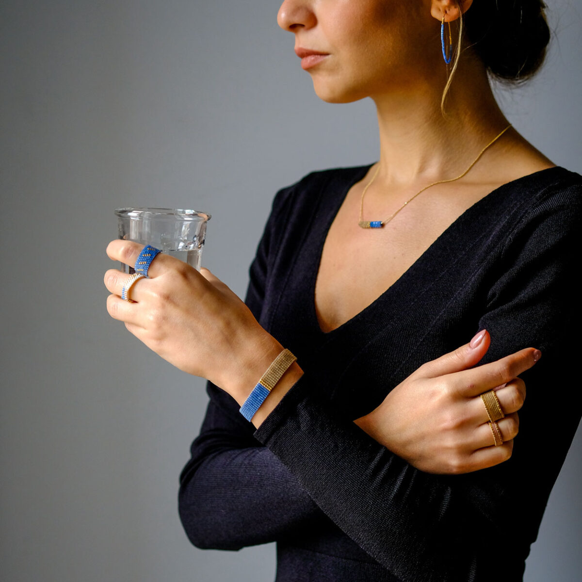 Woman holding a glass of water wearing elegant jewelry and a black dress.