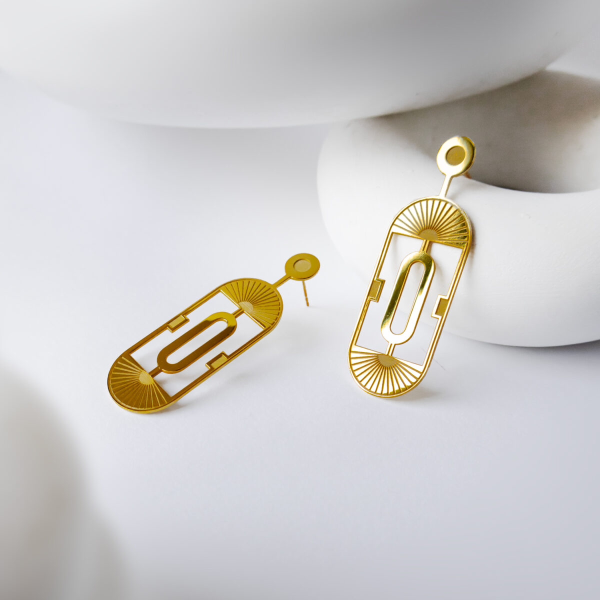 Beyaz bir yüzey üzerinde sergilenen zarif altın art deco tasarımlı küpeler.